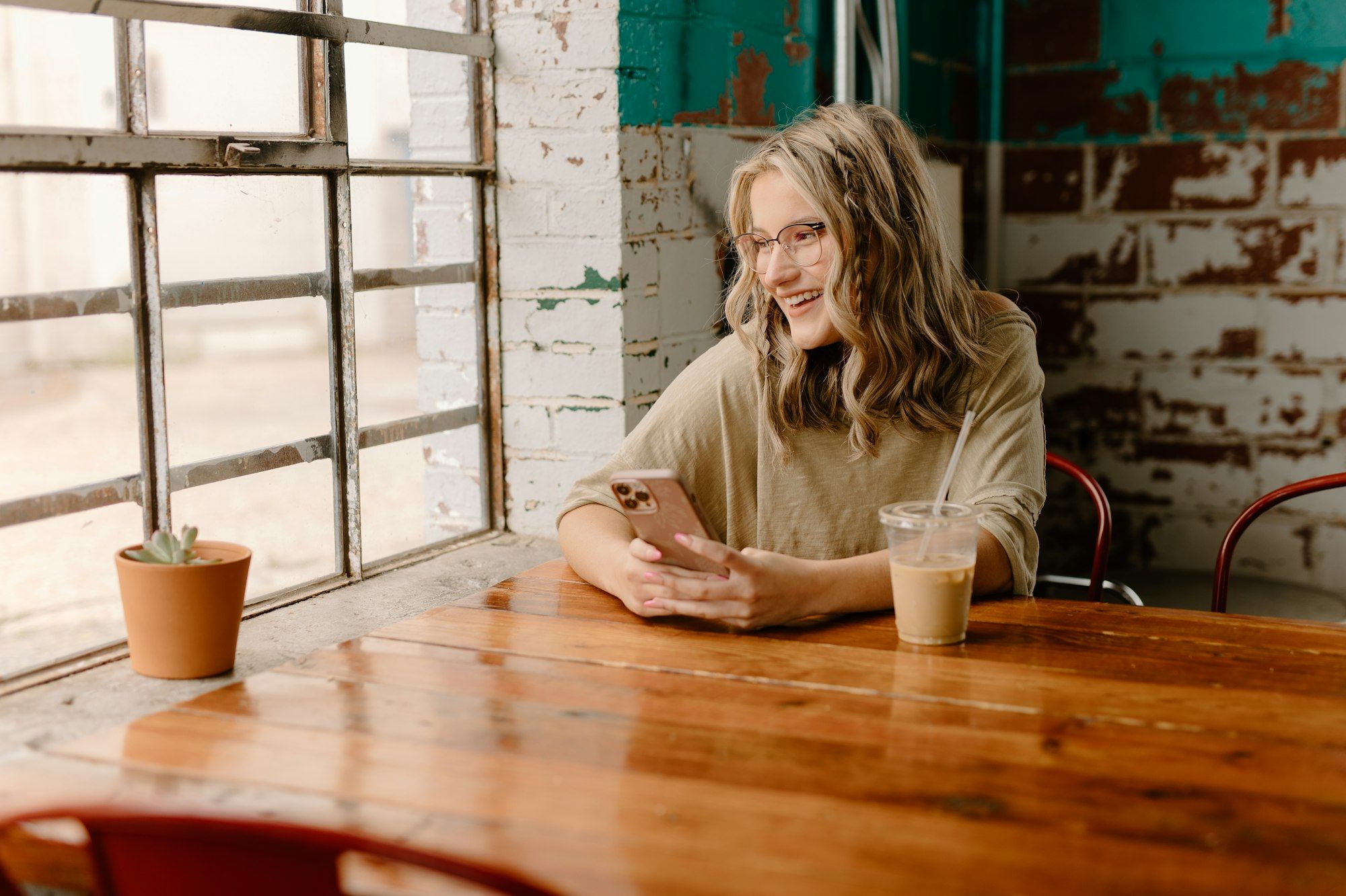 Une cliente consulte son téléphone, souriante, à la table d’un café